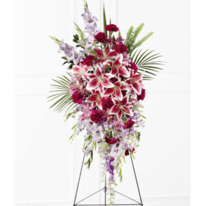 Lavender gladiolus, Stargazer lilies, fuchsia carnations, purple larkspur, lavender Peruvian lilies, lavender chrysanthemums, sword fern fronds, emerald palm fronds and other assorted greens are gorgeously arranged to create a sophisticated standing spray