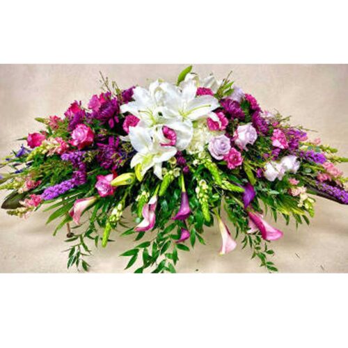 A purple and white sympathy Casket Spray featuring snapdragons, roses, callas lilies, and stock. It's a joyful expression of sympathy sure to be appreciated